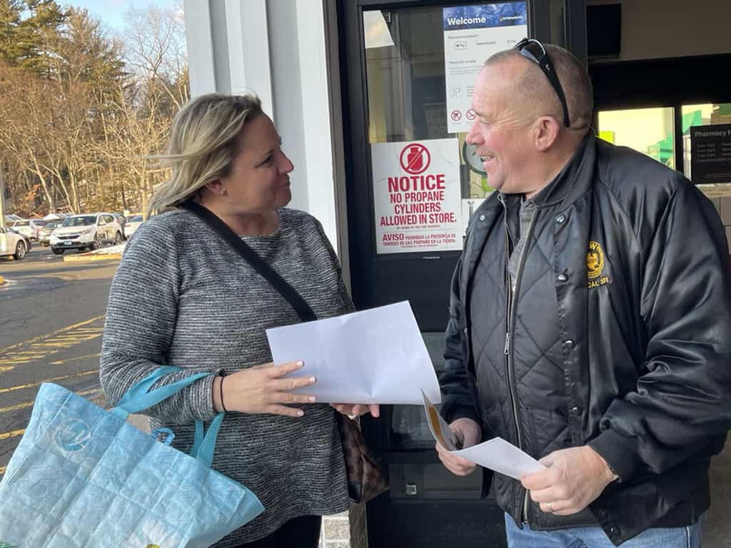 Union workers talking outside store with documents in hand.