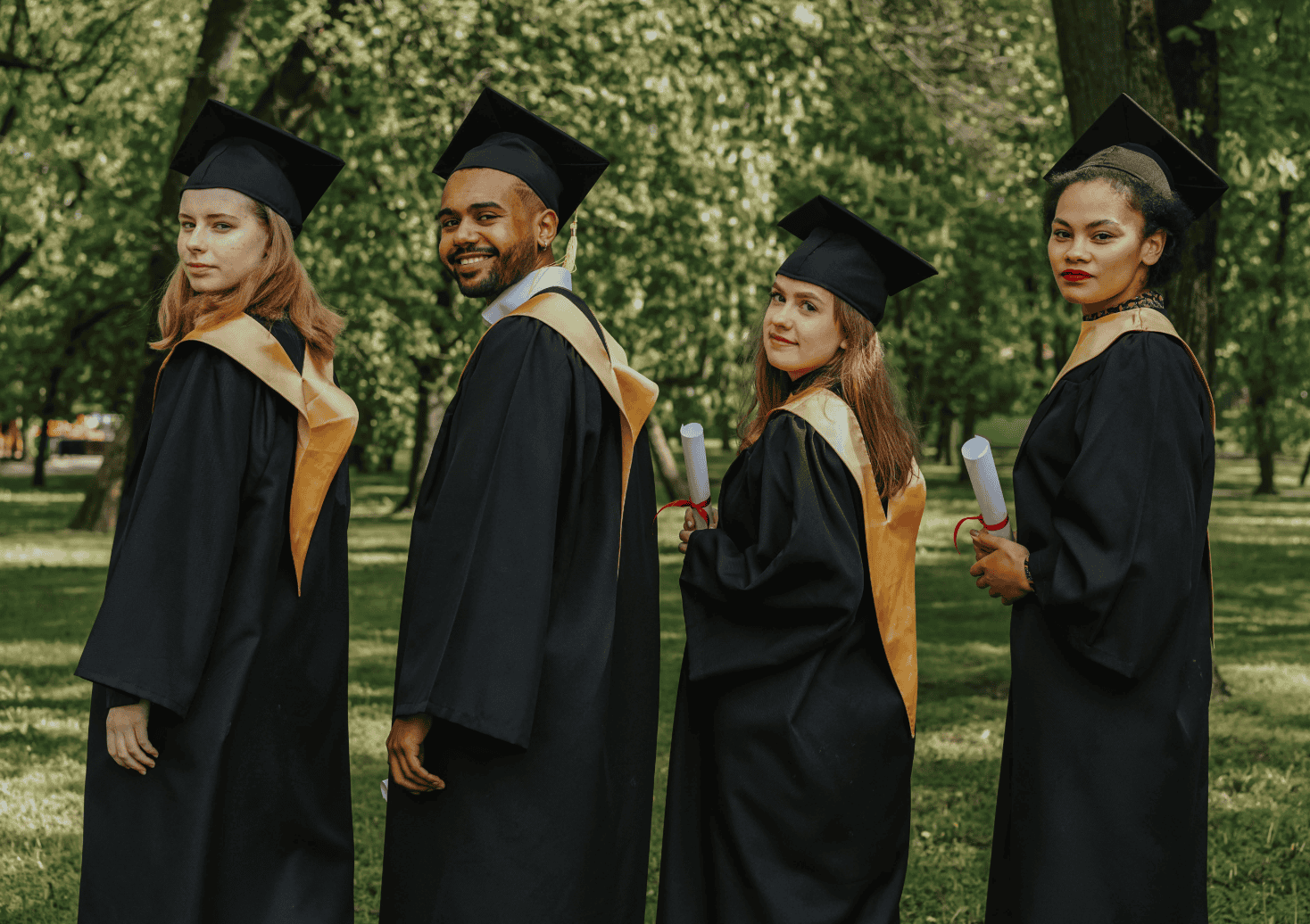 Group of diverse graduates in caps and gowns outdoors.