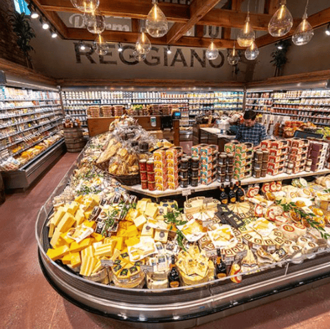 Grocery store display with cheese, jams, and baked goods in a well-lit supermarket aisle.