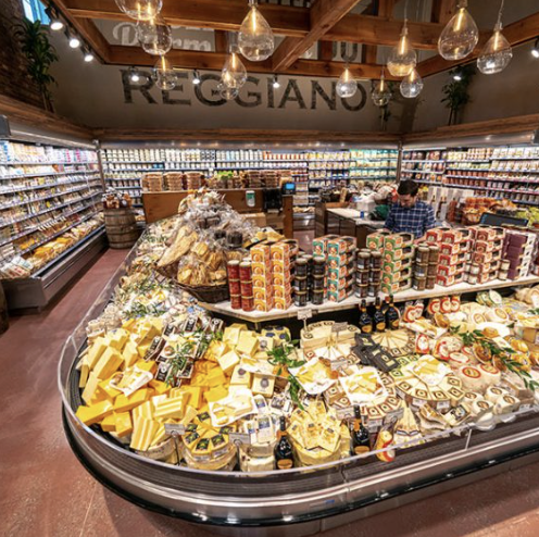 Grocery store display with cheese, jams, and baked goods in a well-lit supermarket aisle.