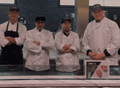 Four chefs in white uniforms and black hats standing behind a food counter at UFCW 371 site.