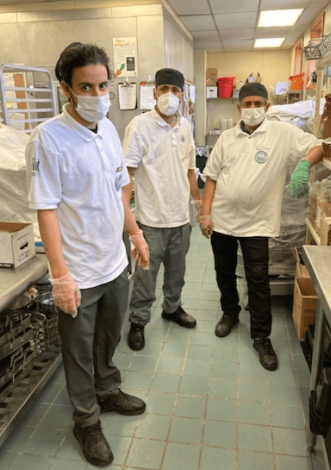Kitchen staff wearing masks and gloves in a commercial kitchen.