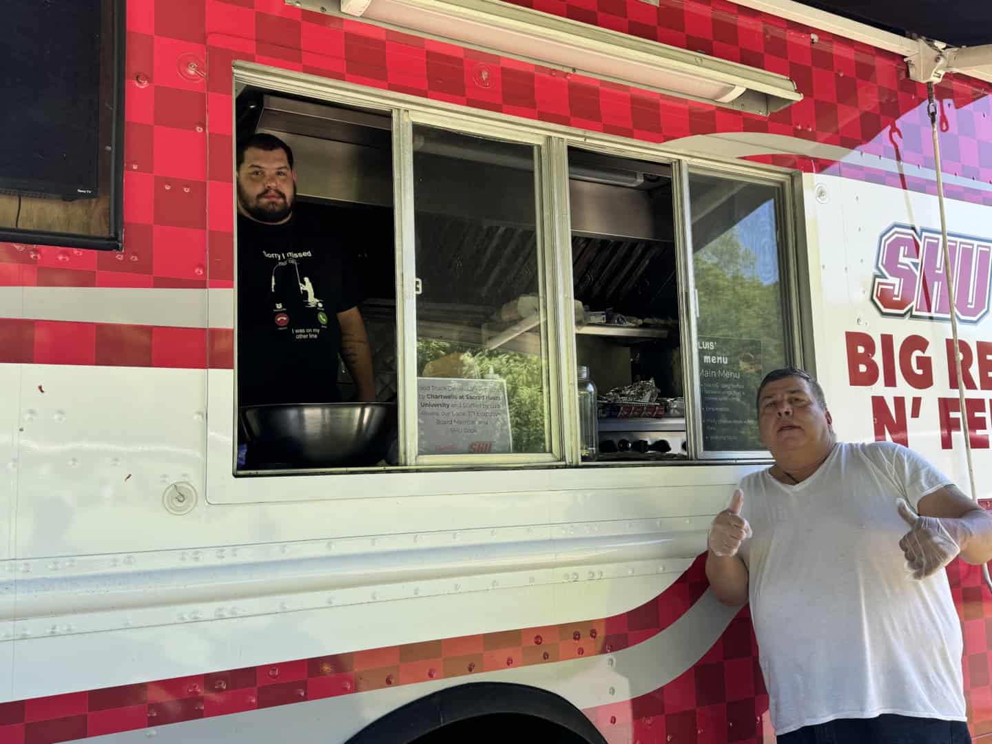Food truck with two staff members, one giving thumbs up, outdoor setting.