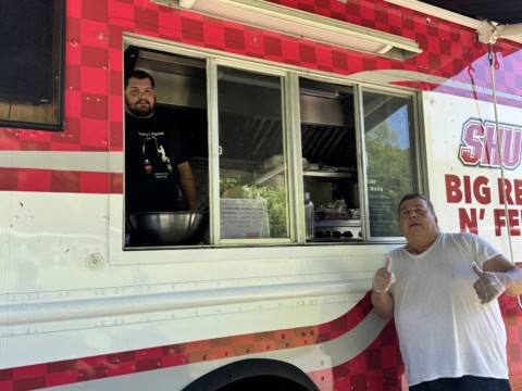 Food truck with two staff members, one giving thumbs up, outdoor setting.