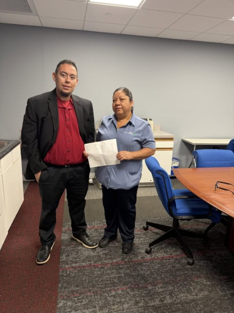 Two union members standing in an office, holding a document, with conference table and chairs nearby.